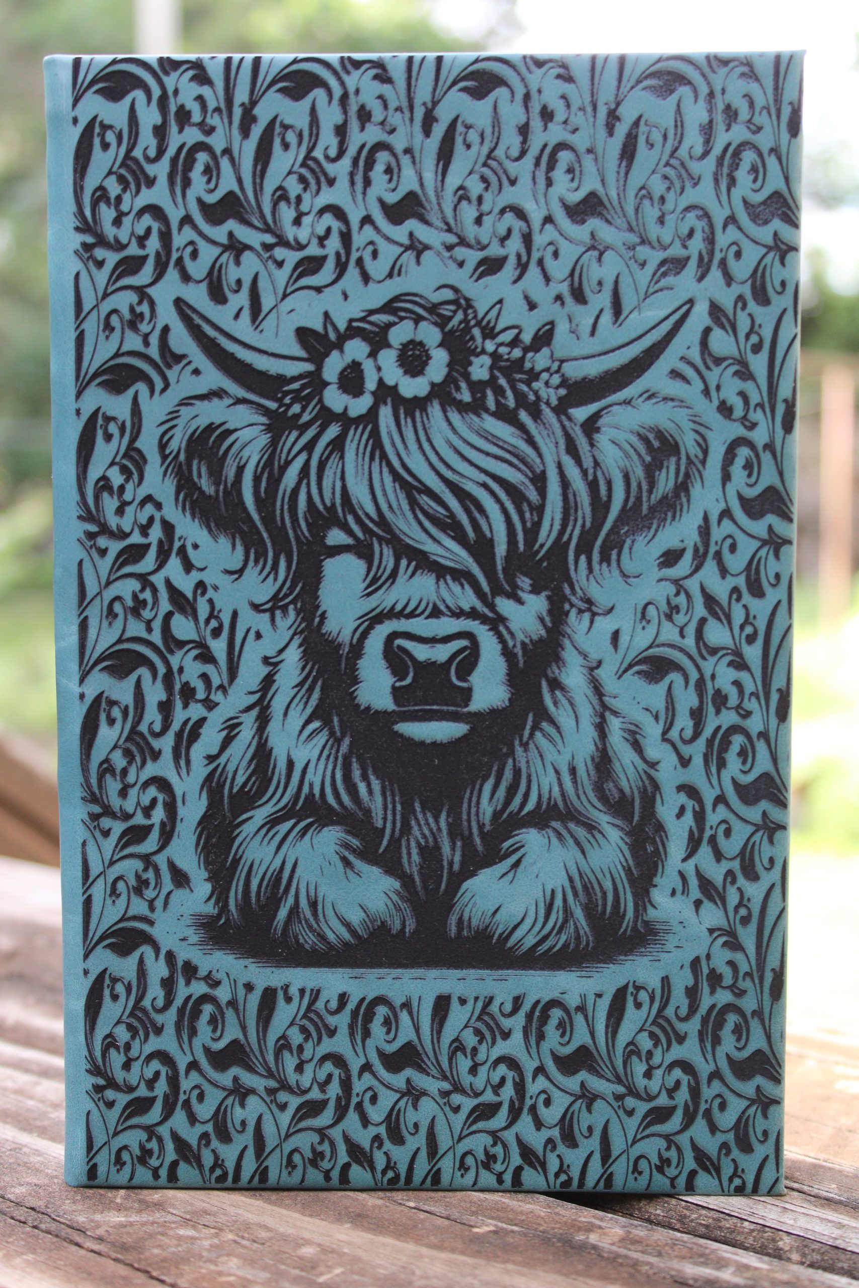 a hardbacked journal with a highland cow and a tooled design around it