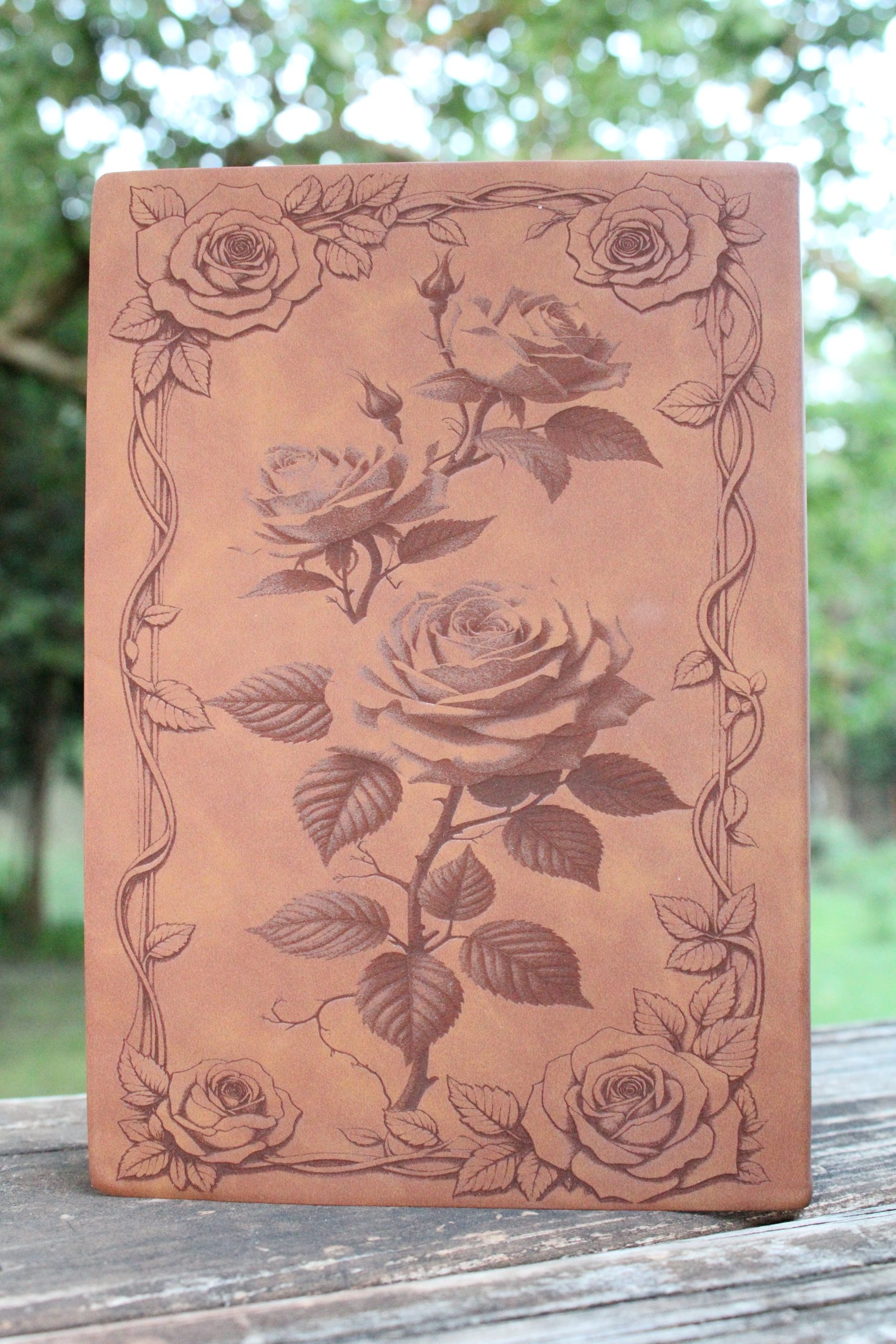 a brown journal with roses as the centerpiece, and a border of roses an vines along the outer edges.