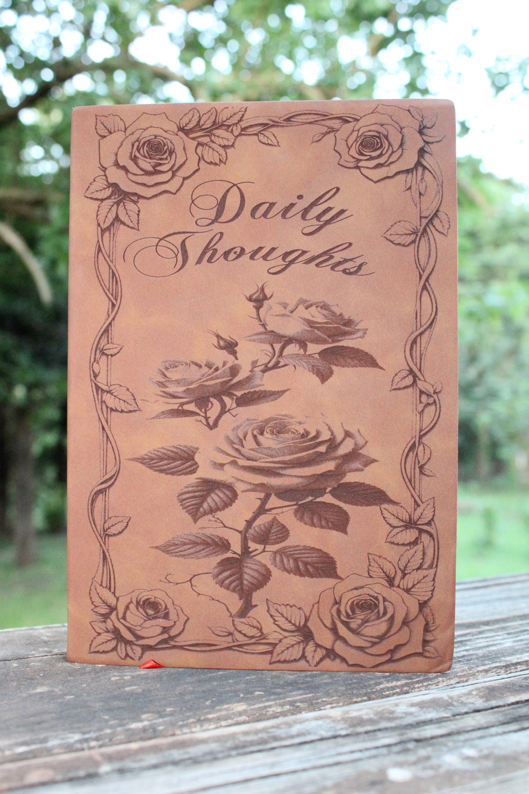 a brown journal with roses as the centerpiece, and a border of roses and vines with 'Daily Thoughts' as the title